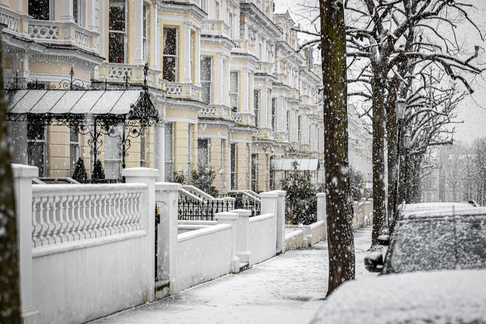 Image of a London street and residential buildings with sash windows during a snow storm, reflecting the importance of sash window heating efficiency for winter.