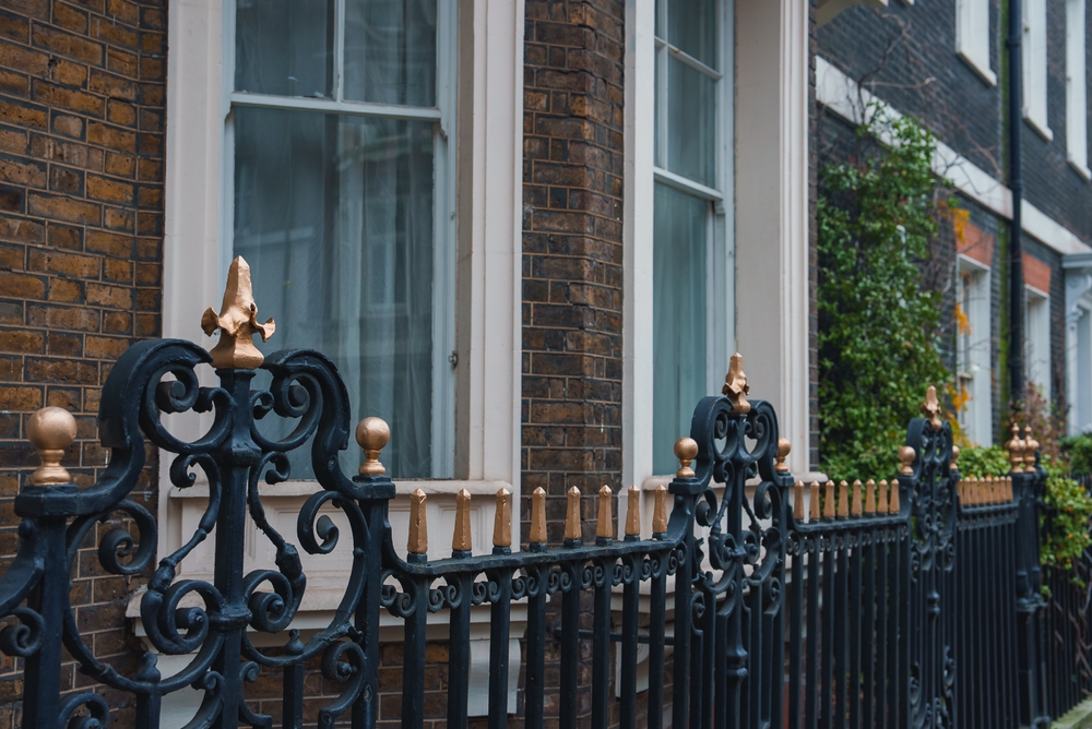 Image of a classic London street, displaying houses with sash windows behind a black and gold gate.